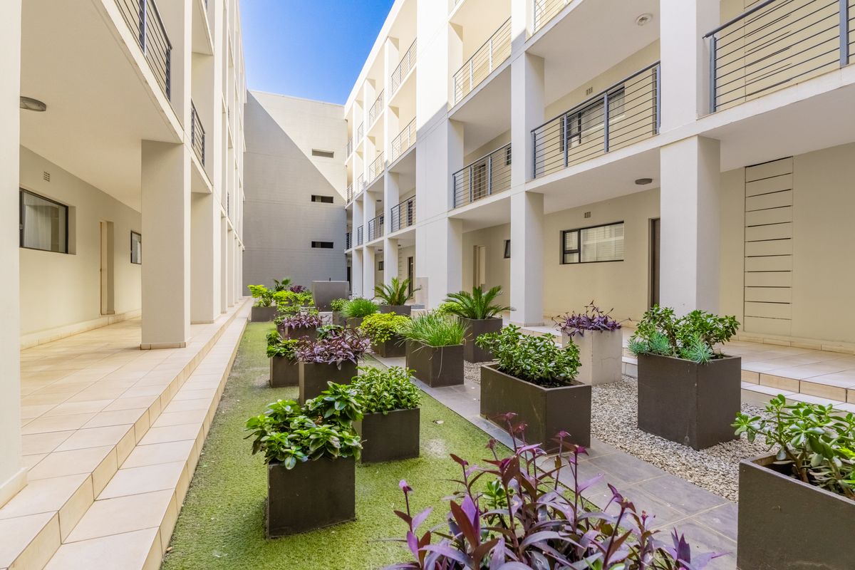 A well-maintained apartment complex courtyard featuring paved walkways, multi-level balconies with balustrades, and landscaped garden planters.