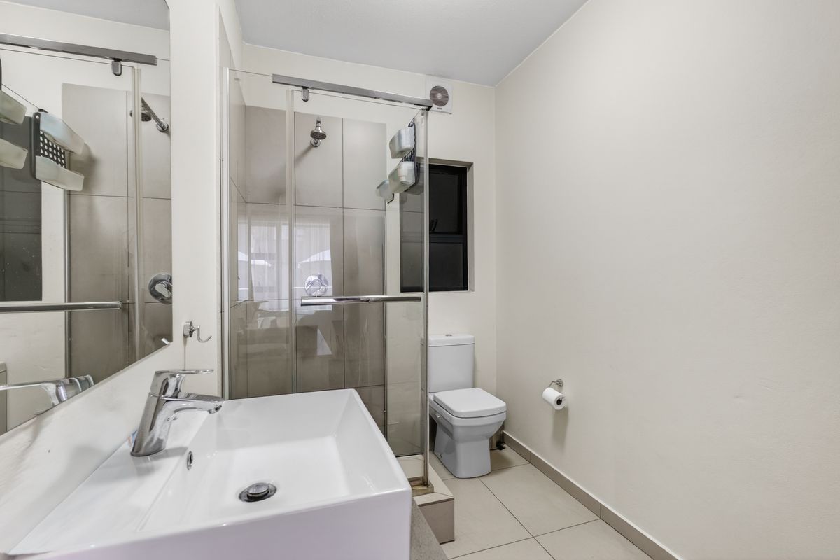 A clean, modern bathroom featuring a glass-enclosed shower, contemporary basin, and neutral tiling throughout.