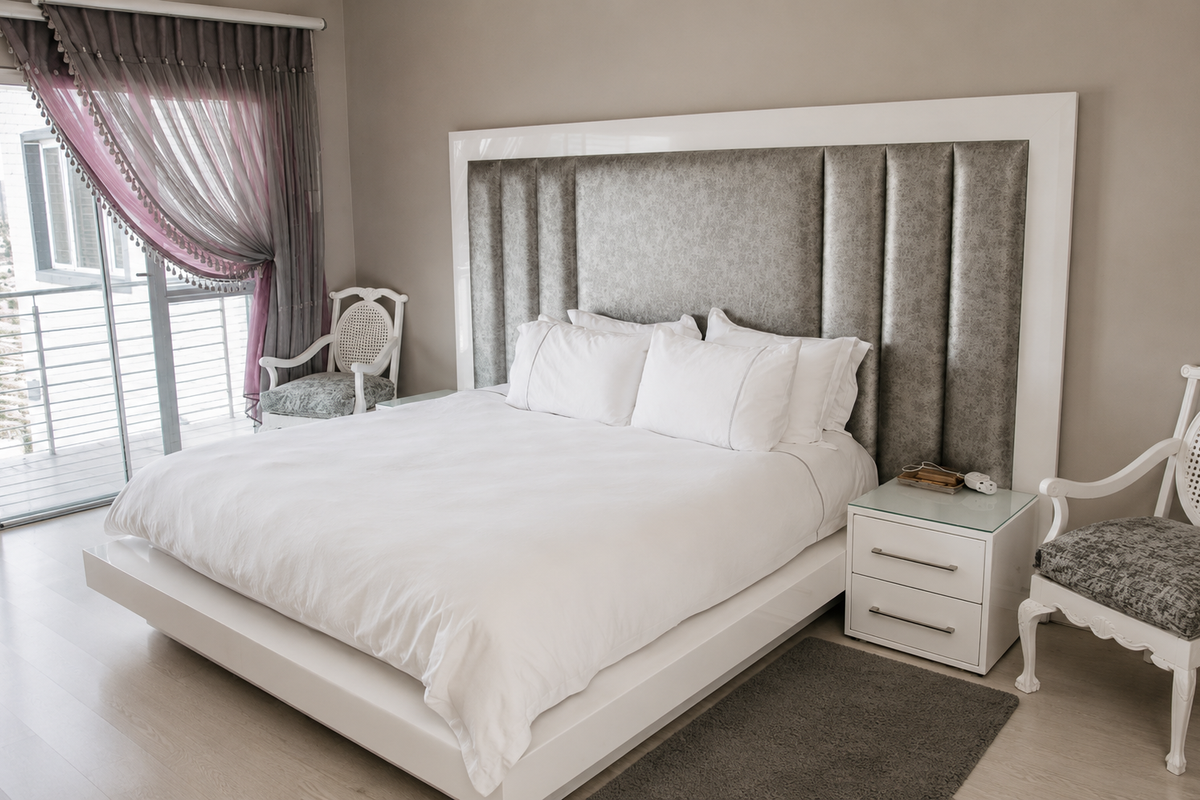 A well-maintained bedroom featuring a large upholstered headboard, laminate flooring, and direct access to a private balcony through sliding glass doors.