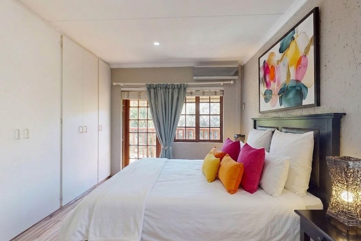 A well-maintained bedroom featuring built-in cupboards, a split-system air conditioner, and direct access to an outdoor balcony through timber-framed doors.