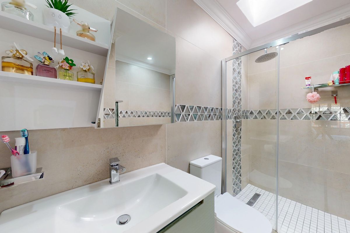 Modern bathroom featuring a walk-in shower with a rain shower head, vanity cabinet with basin, and neutral tiled walls with a decorative mosaic border.
