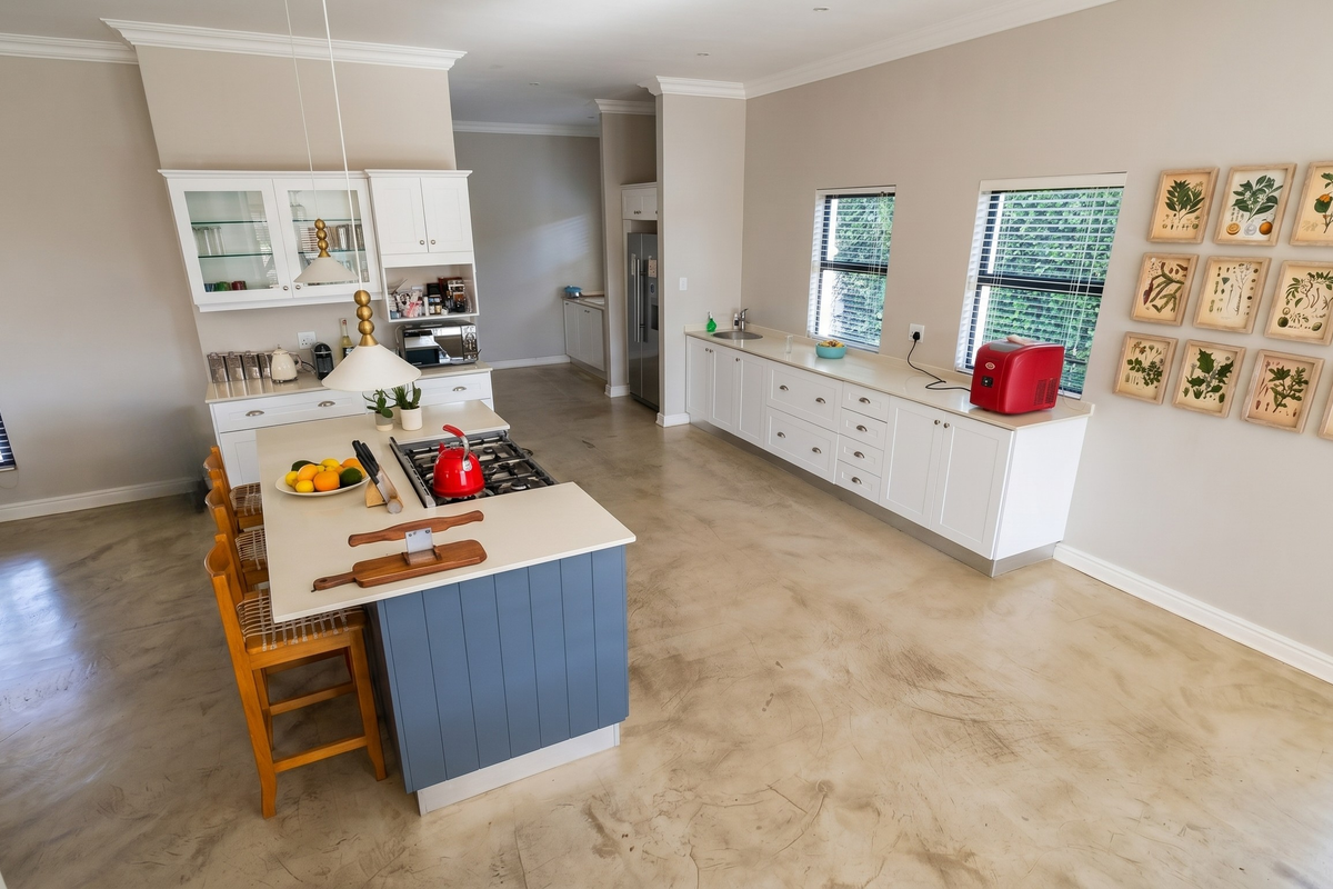 Spacious kitchen featuring a central island with a built-in gas hob, white cabinetry, polished concrete flooring, and ample natural light from multiple windows.