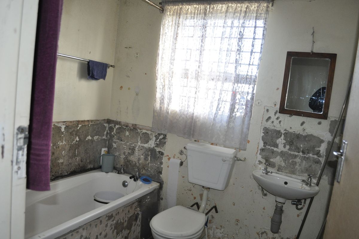 A bathroom in need of significant renovation, featuring a bathtub, toilet, and pedestal basin with extensive wall surface damage.