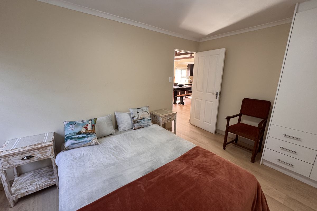 A bedroom featuring light wood-look flooring, built-in white cabinetry, and a doorway leading to an adjacent living area.