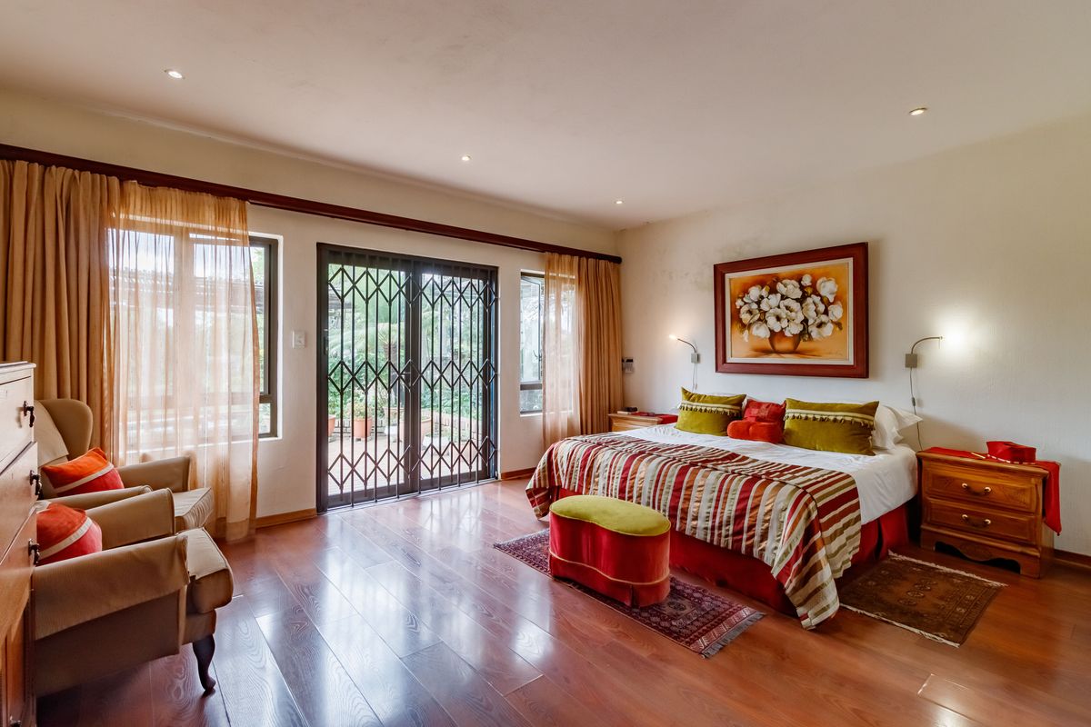 Spacious bedroom featuring warm laminate flooring, recessed lighting, and direct access to an outdoor patio through a sliding glass door with security gate.