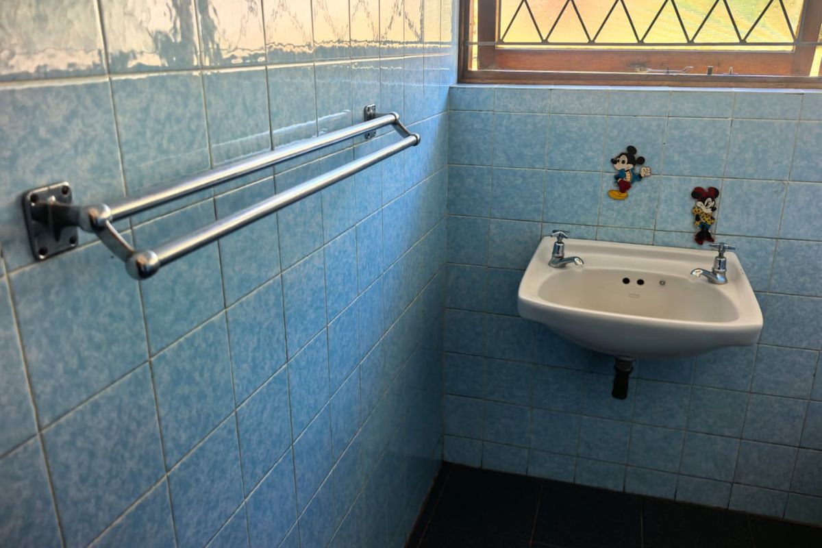 A dated bathroom featuring blue ceramic wall tiles, a wall-mounted basin with chrome fixtures, and a leaded glass window.