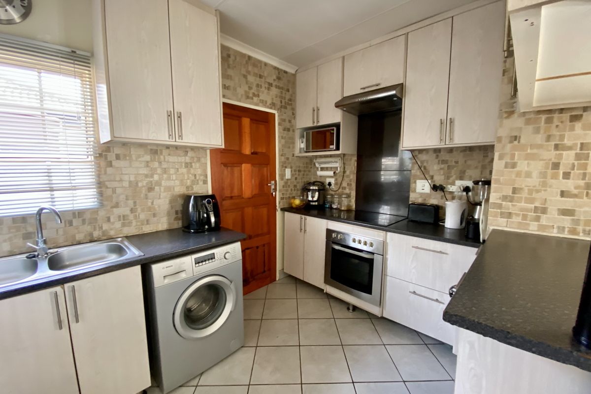 Functional kitchen featuring light-toned cabinetry, dark countertops, integrated oven, extractor fan, and tiled flooring with a dedicated space for a washing machine.