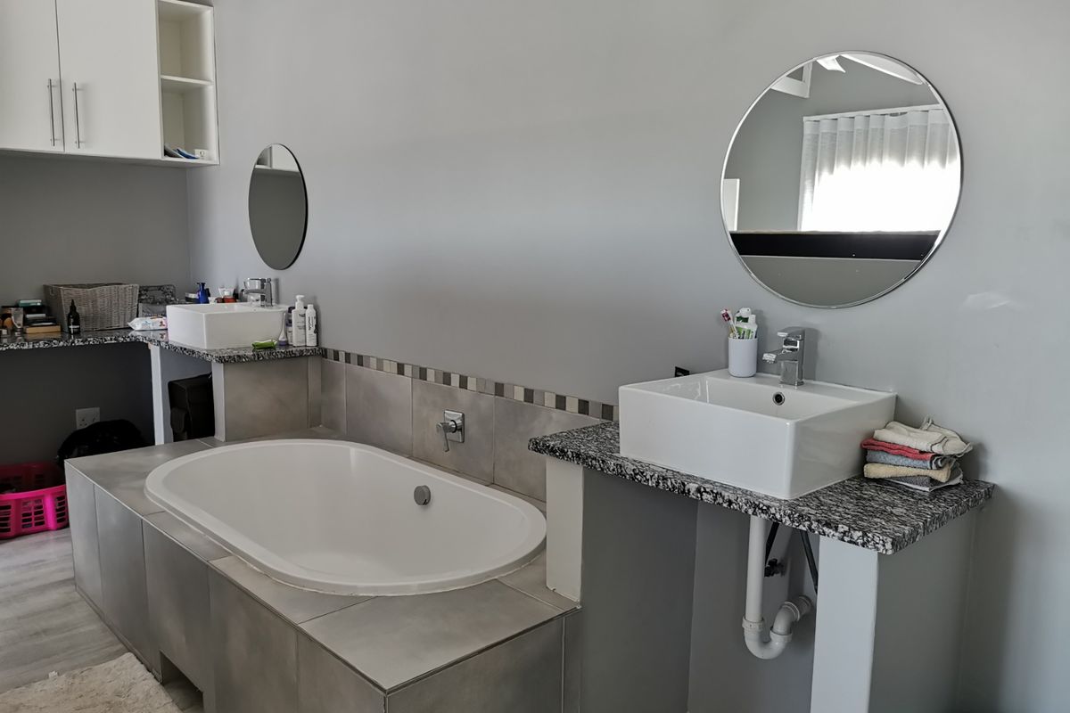 A modern bathroom featuring a built-in bathtub, dual vessel sinks on granite countertops, and wall-mounted cabinetry with contemporary finishes.