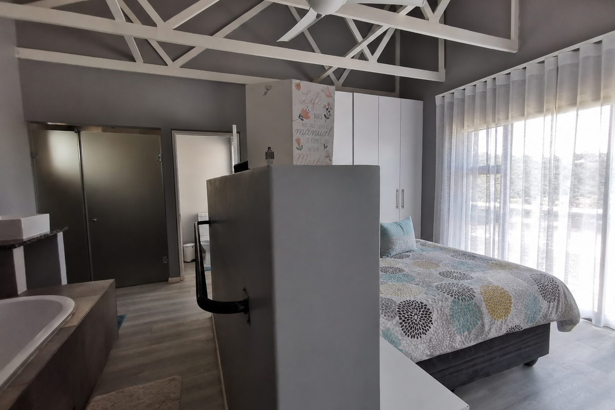 Spacious bedroom featuring exposed roof trusses, built-in cupboards, and an open-plan en-suite bathroom with a freestanding bathtub and modern laminate flooring.