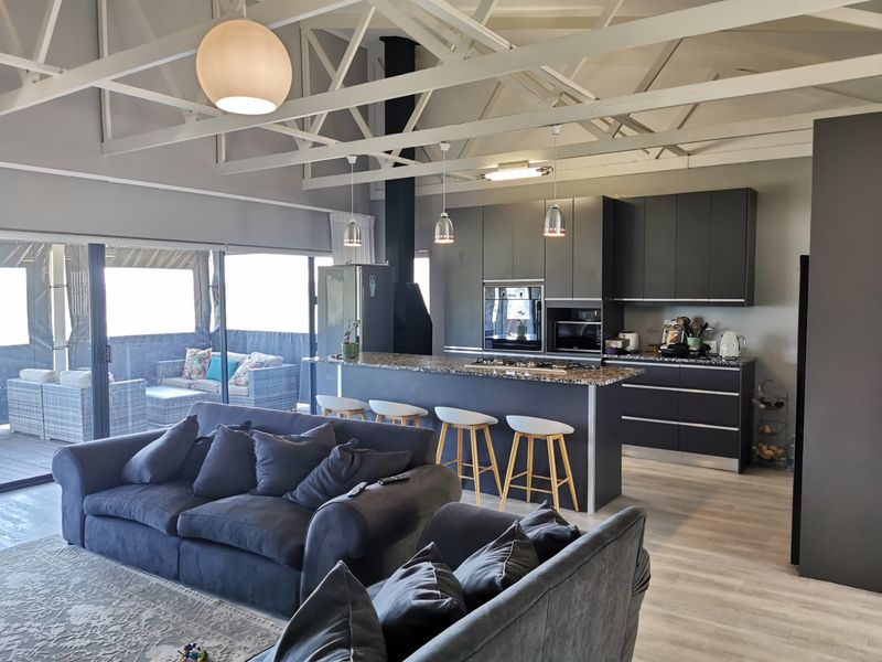 Spacious open-plan living area featuring a modern kitchen with granite island, built-in appliances, exposed roof trusses, and seamless flow to the outdoor patio.