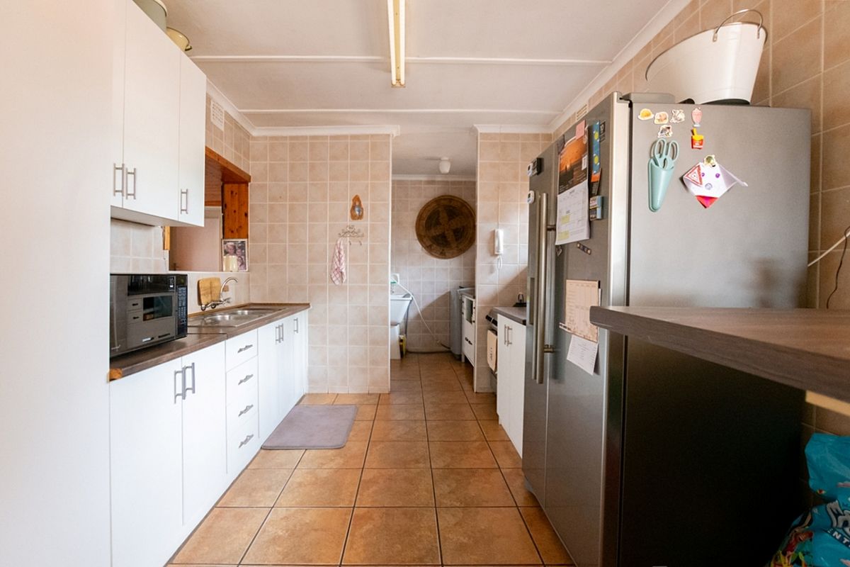A functional kitchen featuring white cabinetry, tiled splashbacks, and tiled flooring, with a connected scullery area visible in the background.