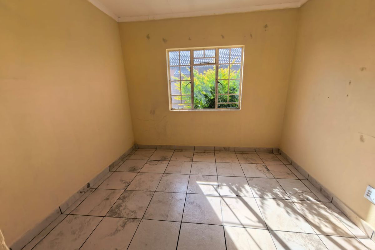 An empty bedroom featuring tiled flooring and a steel-framed window, requiring cosmetic updates to the walls and flooring.