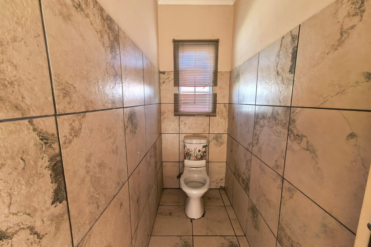 A compact, fully tiled bathroom featuring a standard toilet and a small window with fitted blinds.