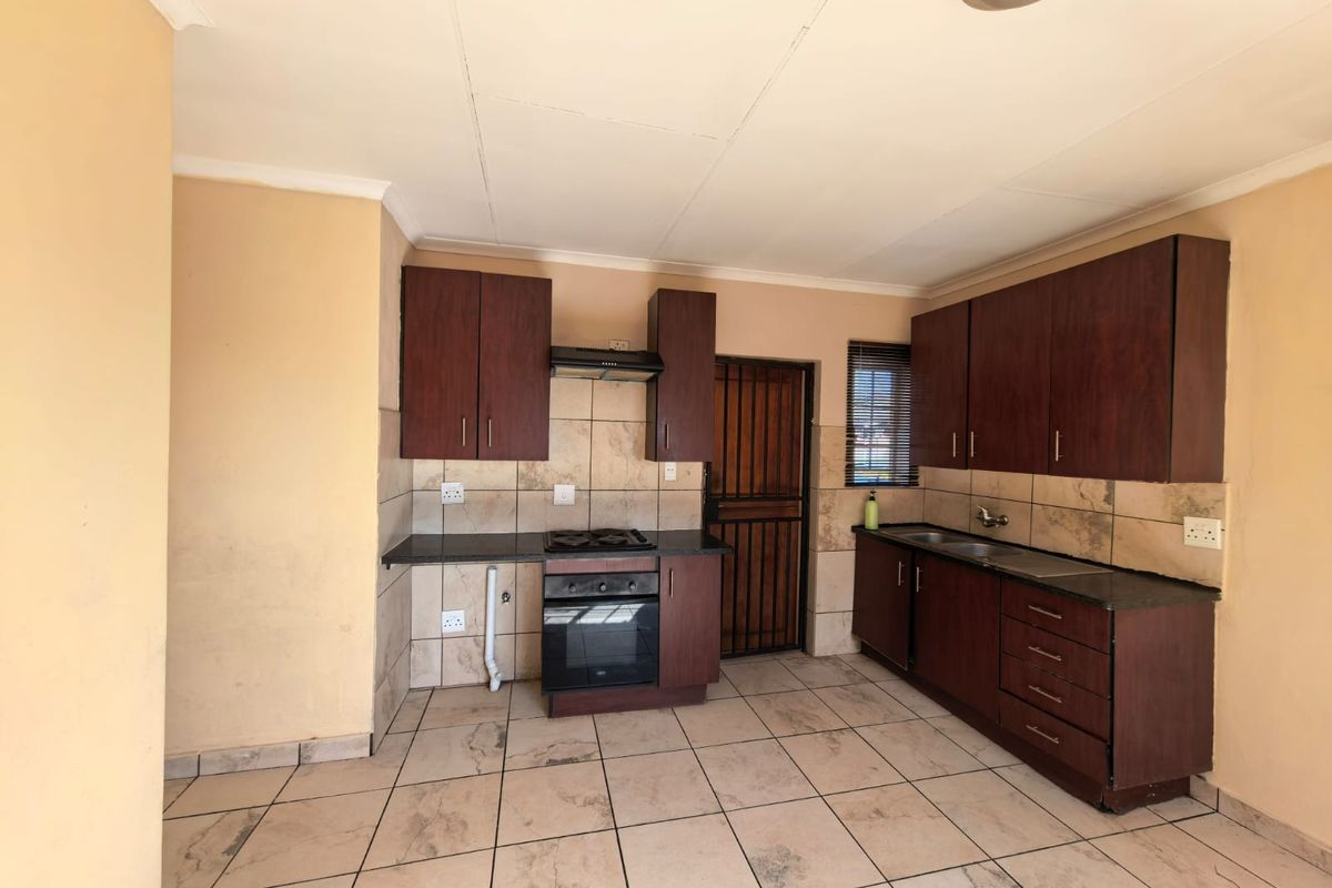 A functional kitchen featuring dark wood cabinetry, granite countertops, built-in oven, gas hob, and tiled finishes throughout.