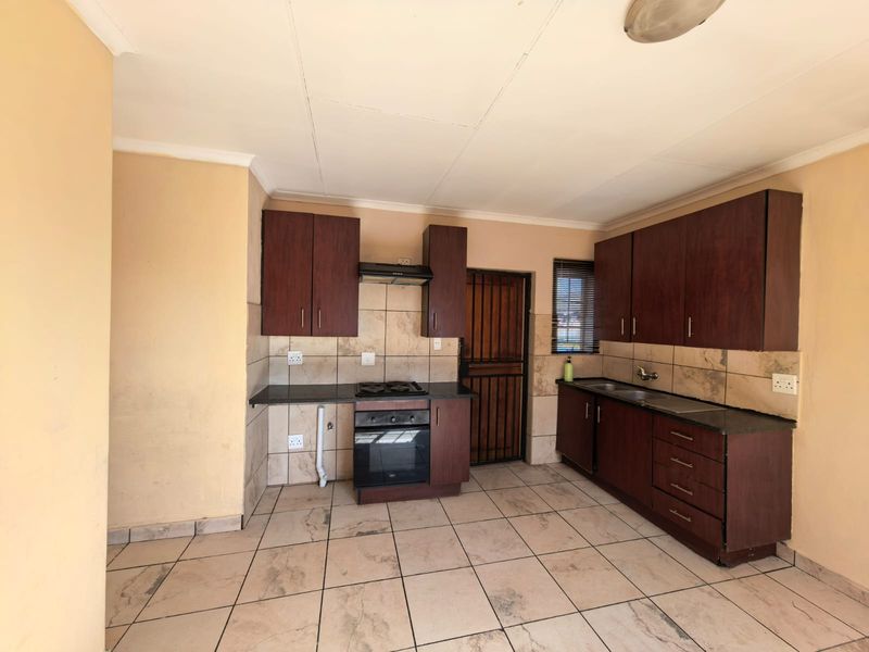 A functional kitchen featuring dark wood cabinetry, granite countertops, built-in oven, gas hob, and tiled finishes throughout.
