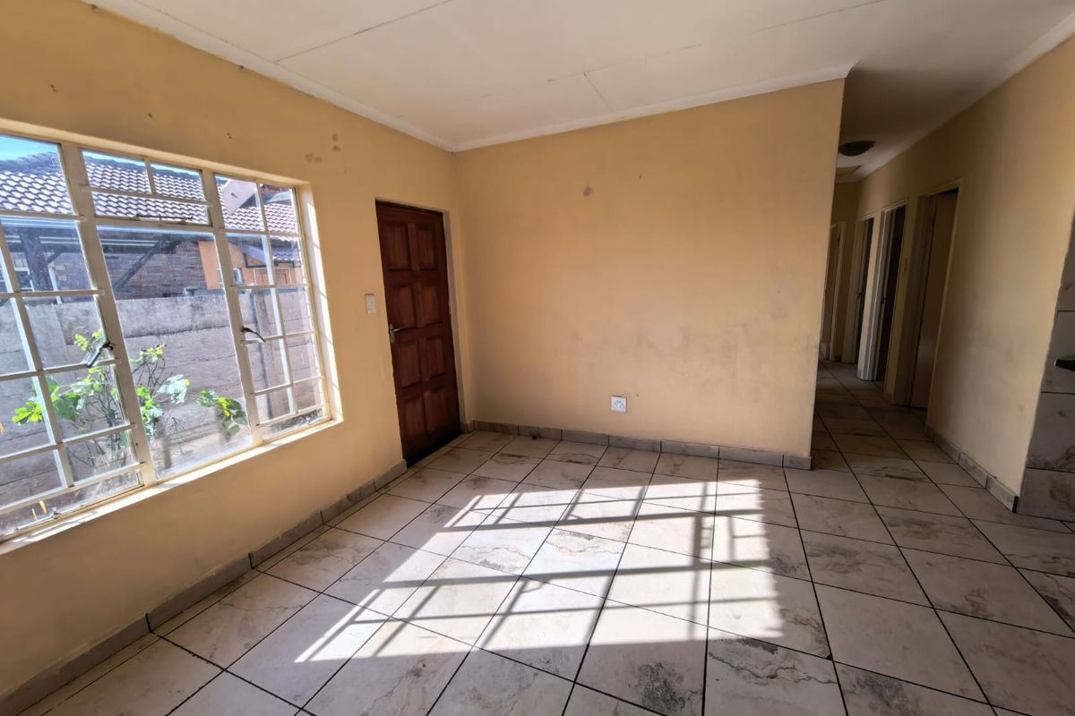 An empty living area featuring tiled flooring, a steel-framed window, and a timber door, requiring cosmetic updates to improve its overall condition.