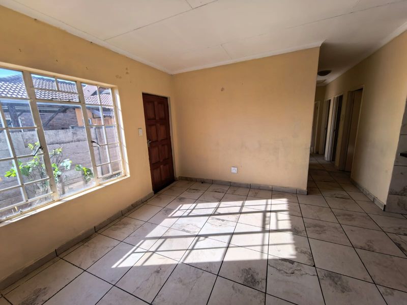 An empty living area featuring tiled flooring, a steel-framed window, and a timber door, requiring cosmetic updates to improve its overall condition.