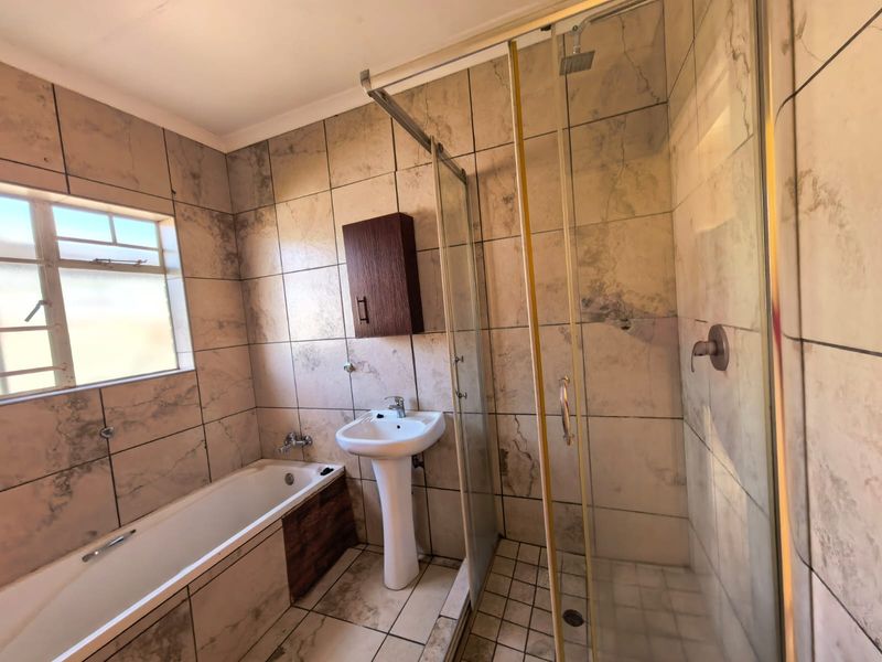 A functional bathroom featuring a pedestal basin, bathtub, and separate shower enclosure with full-height wall tiling.