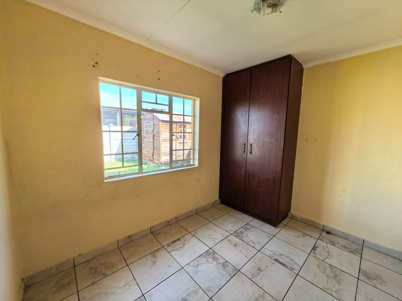 A vacant bedroom featuring tiled flooring, a built-in wooden wardrobe, and a steel-framed window overlooking the rear yard.