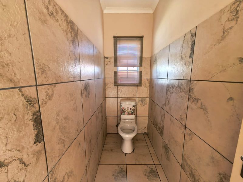 A compact, fully tiled bathroom featuring a standard toilet and a small window with fitted blinds.