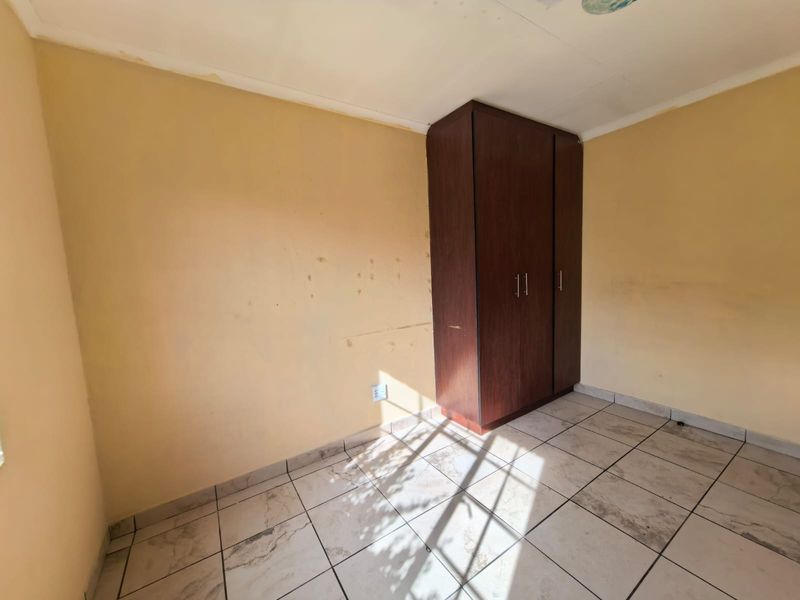 A vacant bedroom featuring tiled flooring and a built-in wooden wardrobe, requiring cosmetic updates to the wall finishes.