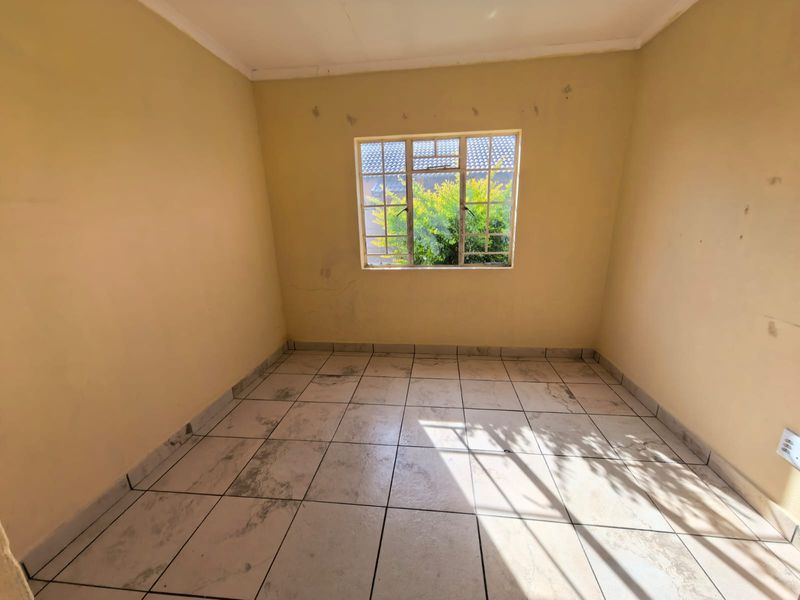 An empty bedroom featuring tiled flooring and a steel-framed window, requiring cosmetic updates to the walls and flooring.