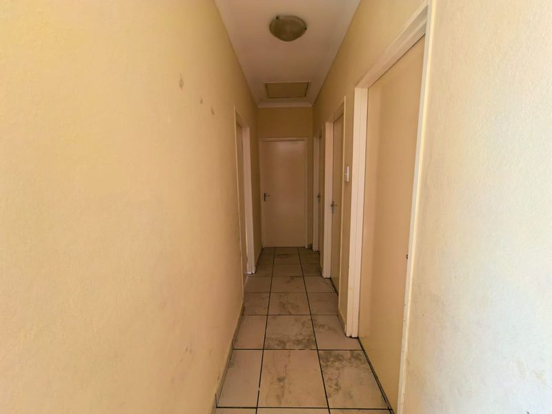 A functional hallway featuring tiled flooring and multiple internal doors, showing signs of wear on the walls and floor surfaces.