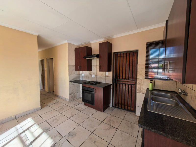 A functional kitchen featuring built-in cabinetry, a hob, oven, extractor fan, and double sink, with tiled flooring and direct access to an exterior security door.