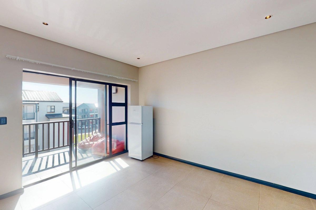 A bright, open-plan living area featuring neutral tiled flooring, recessed lighting, and large sliding glass doors leading to a private balcony.