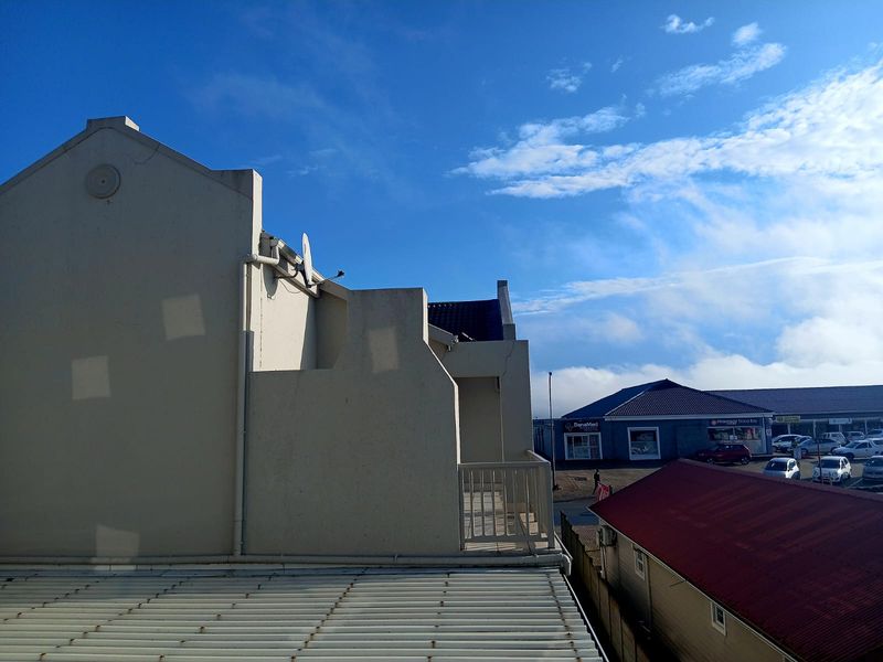 View of the rear building elevation featuring a balcony, corrugated metal roofing, and a satellite dish, overlooking a nearby commercial area.