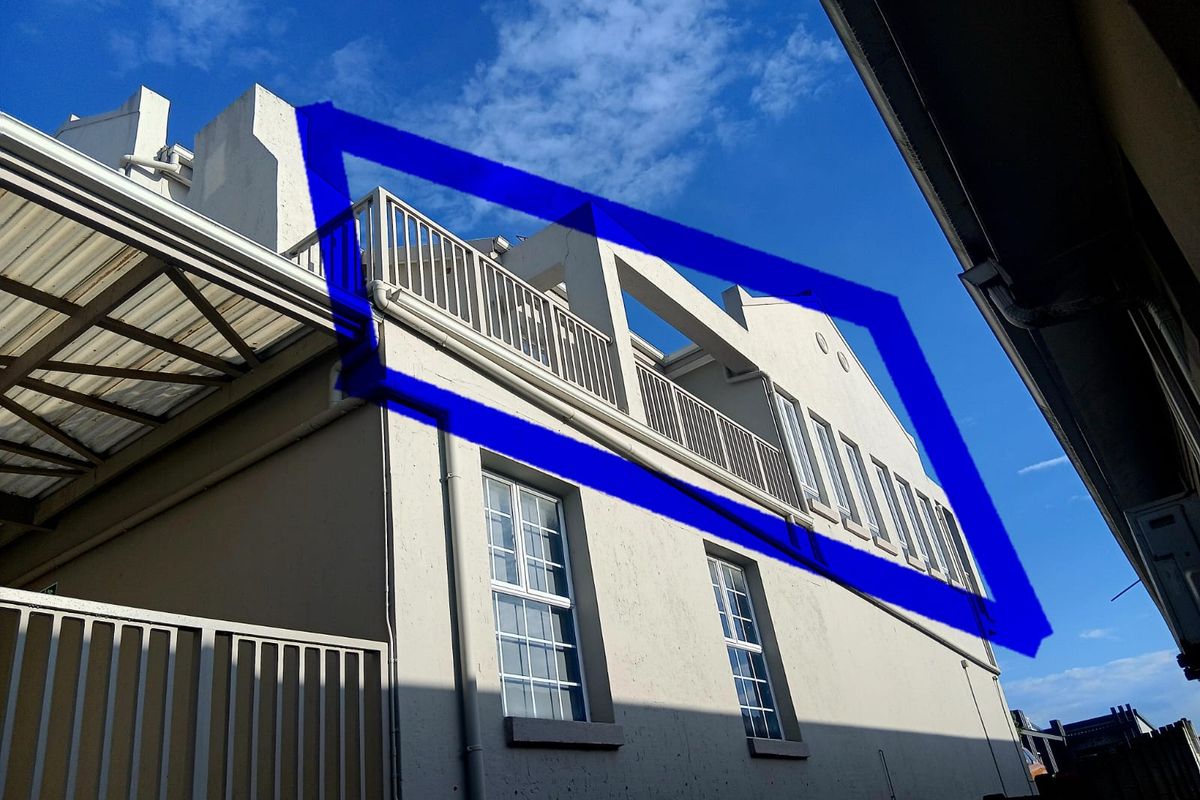 Exterior view of the apartment building featuring a balcony with metal railings and multiple casement windows against a clear blue sky.