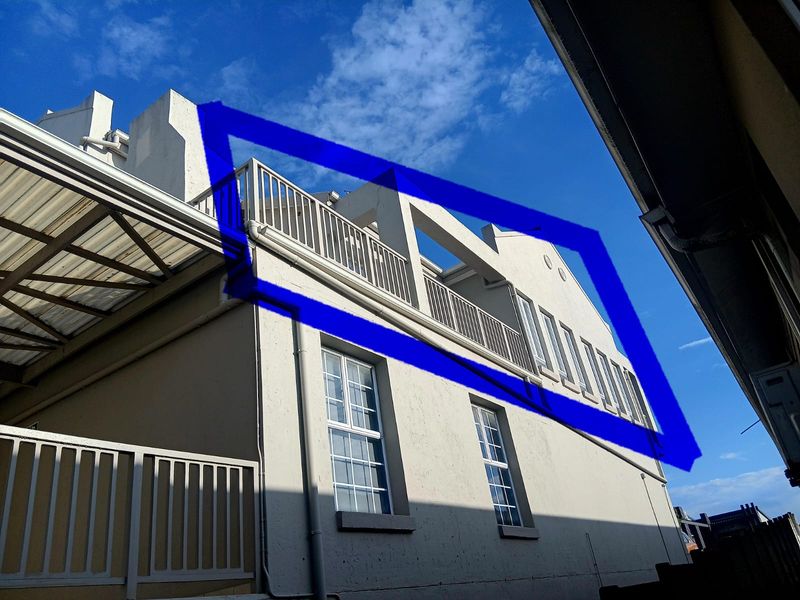 Exterior view of the apartment building featuring a balcony with metal railings and multiple casement windows against a clear blue sky.