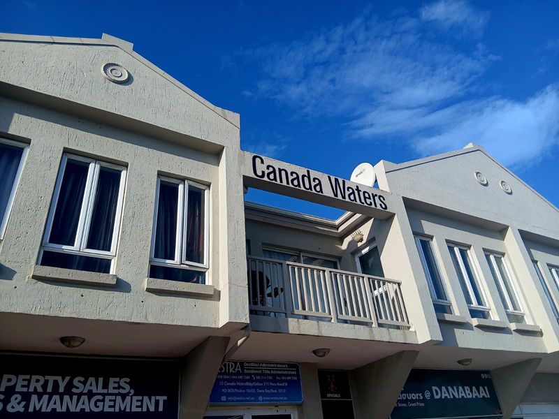 Front elevation of the Canada Waters apartment building featuring a balcony, textured facade, and commercial signage at the ground level.