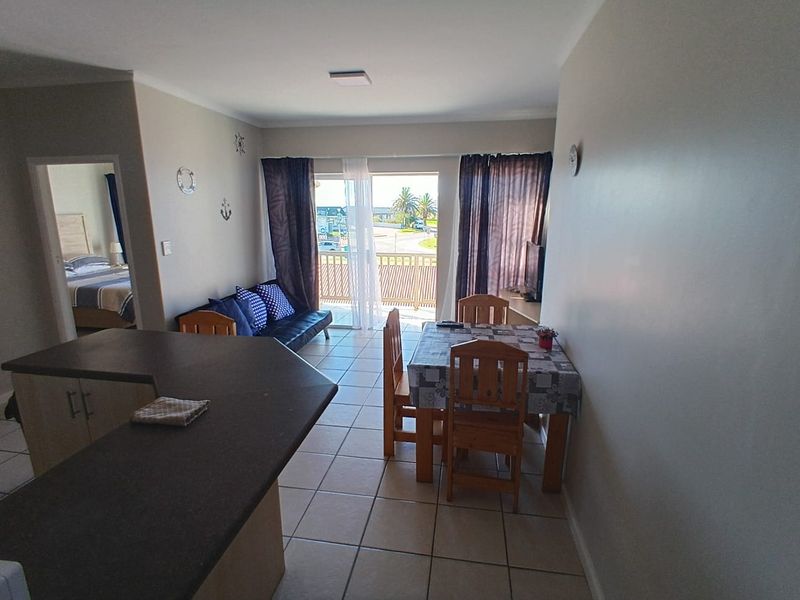 Open-plan living and dining area featuring tiled flooring, a kitchen breakfast bar, and direct access to a balcony with exterior views.
