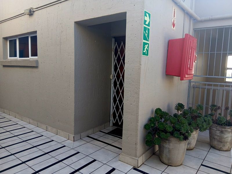 Exterior common area featuring tiled flooring, a security gate entrance, and wall-mounted fire safety equipment.
