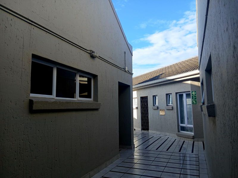 A paved exterior walkway between apartment building sections, featuring tiled flooring, security gates, and external lighting fixtures.