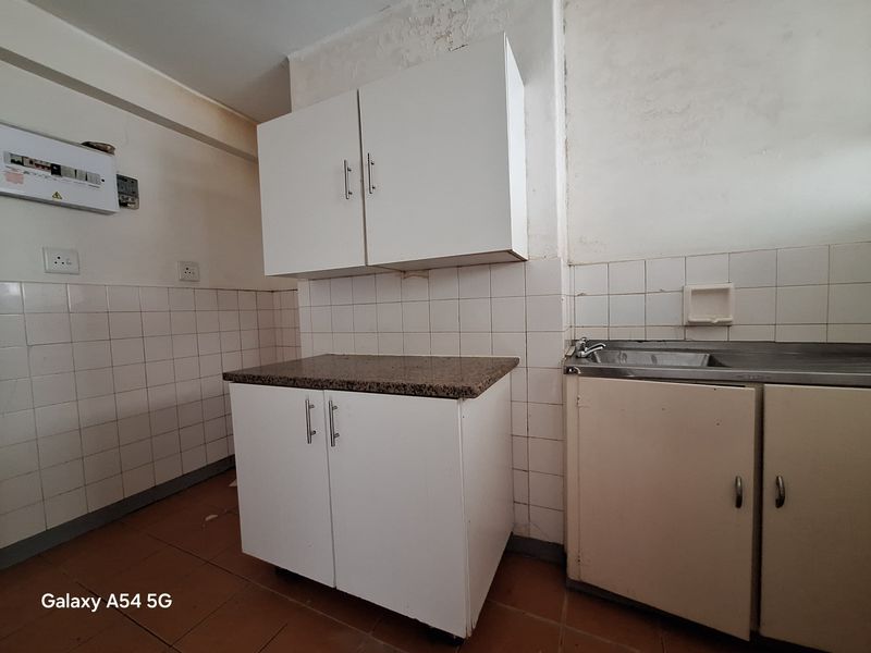 A compact kitchen area featuring basic built-in cabinetry, a granite countertop, and a stainless steel sink, requiring cosmetic updates and repairs.
