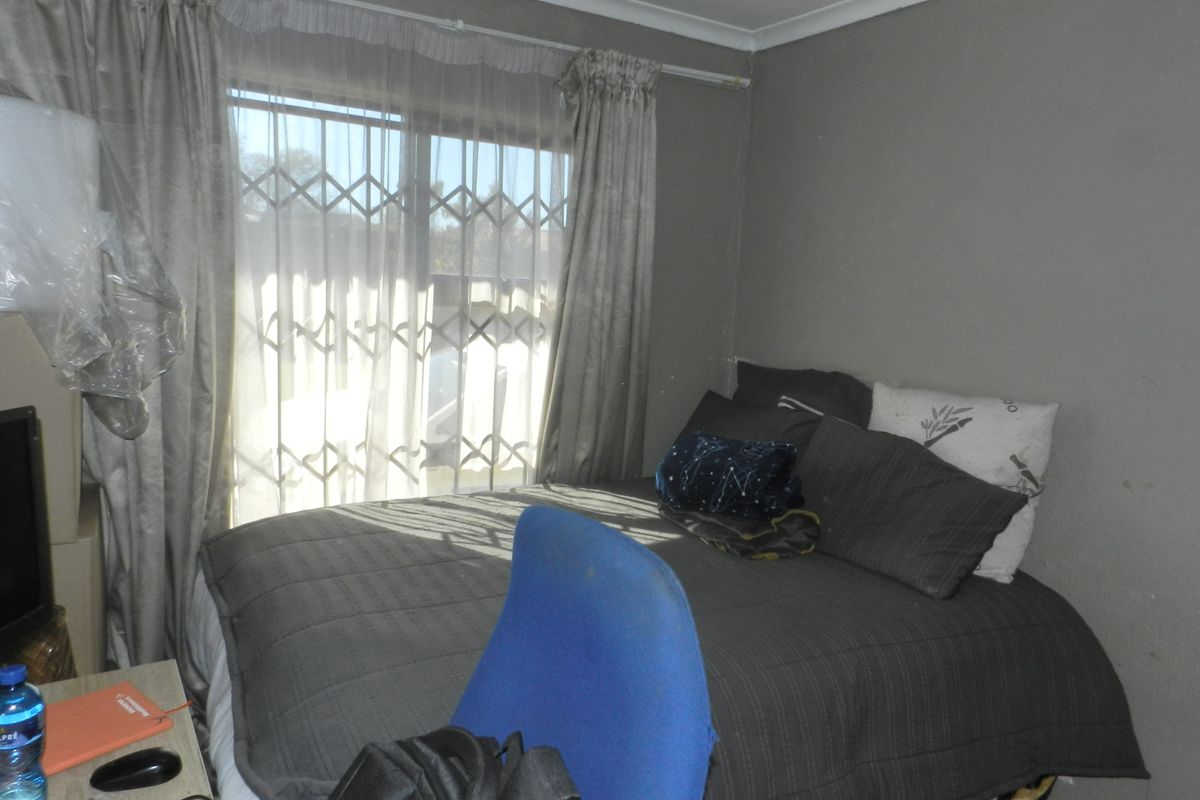 A bedroom featuring a window with a security gate and curtain rails, finished with simple coving.
