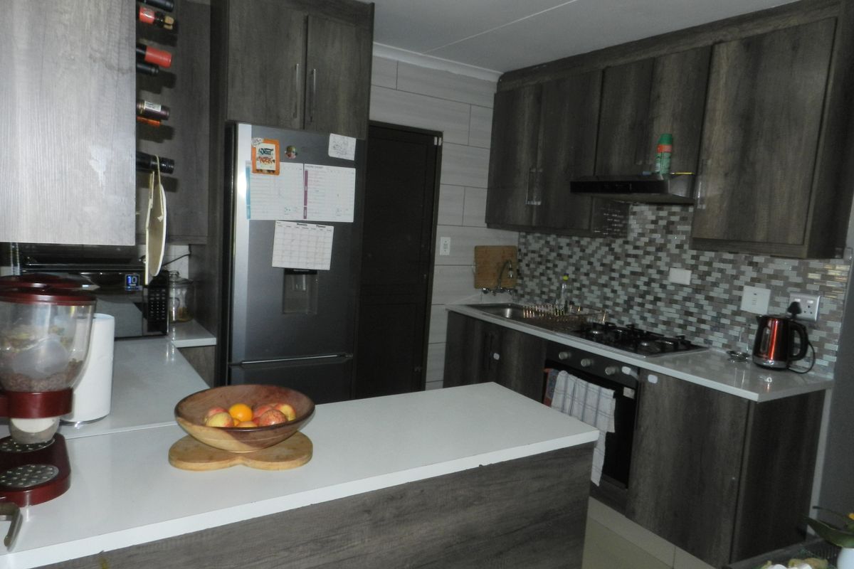 Modern kitchen featuring dark wood-grain cabinetry, stone countertops, a gas hob with extractor fan, and a decorative mosaic tile backsplash.