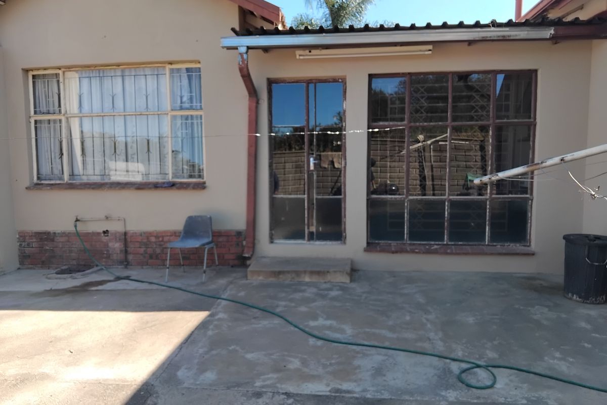 Rear exterior view of the house featuring a concrete patio, steel-framed windows, and brick base detailing.