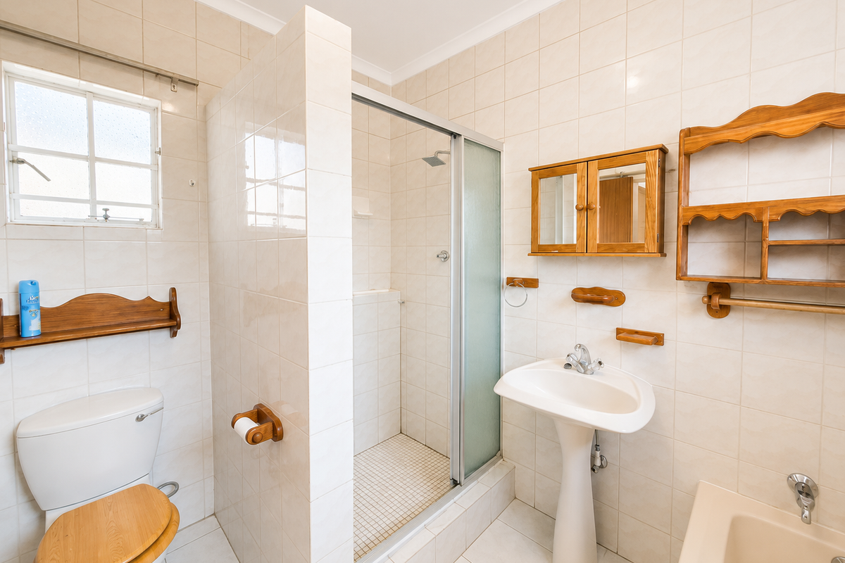 A functional bathroom featuring a pedestal basin, a separate shower enclosure, and a toilet, finished with neutral wall and floor tiling.