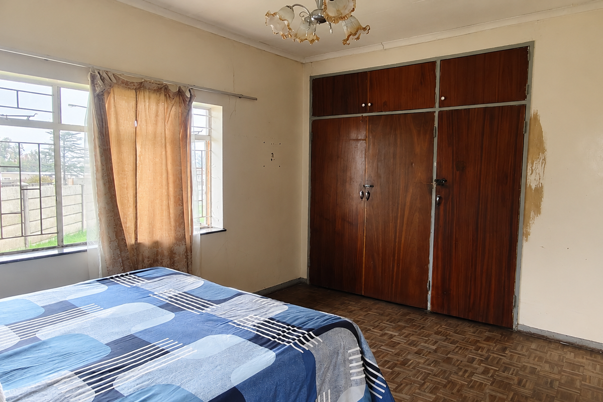A bedroom featuring original parquet flooring, built-in wooden cupboards, and a steel-framed window, requiring cosmetic updates to the wall finishes.