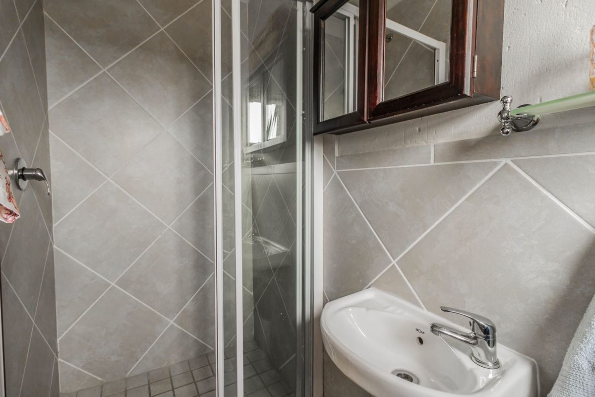 A functional bathroom featuring a shower enclosure, wall-mounted basin with chrome mixer tap, and neutral diamond-patterned wall tiling.