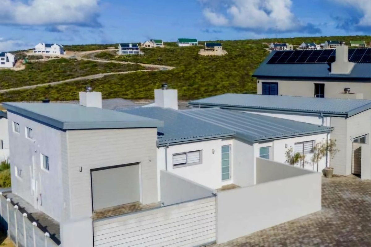 Aerial view of a modern residential property featuring a metal roof, solar panels, paved driveway, and secure boundary walling in a coastal estate setting.