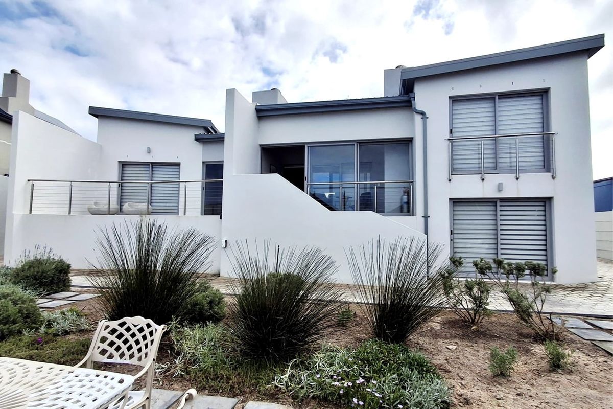 Rear elevation of a modern multi-level home featuring sliding glass doors, stainless steel balustrades, and a paved patio area overlooking a landscaped garden.
