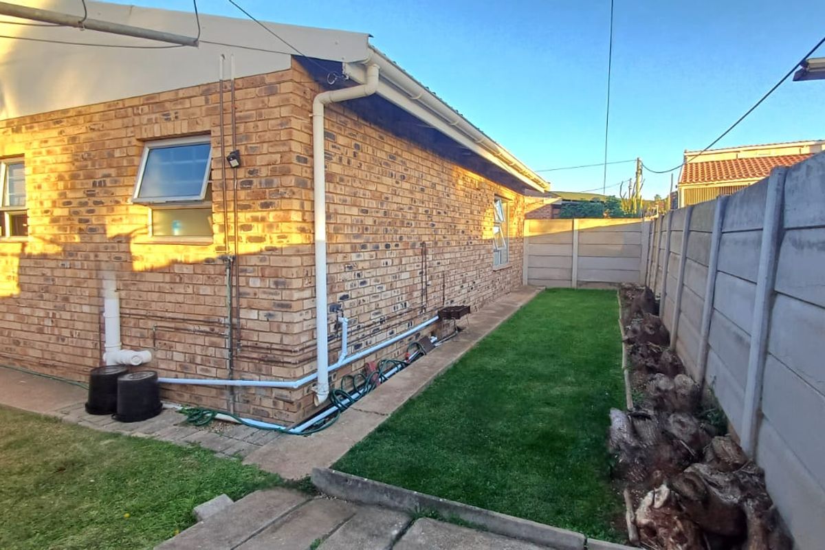 Rear exterior view of the townhouse featuring a face brick facade, a small lawn area, and a precast concrete boundary wall.