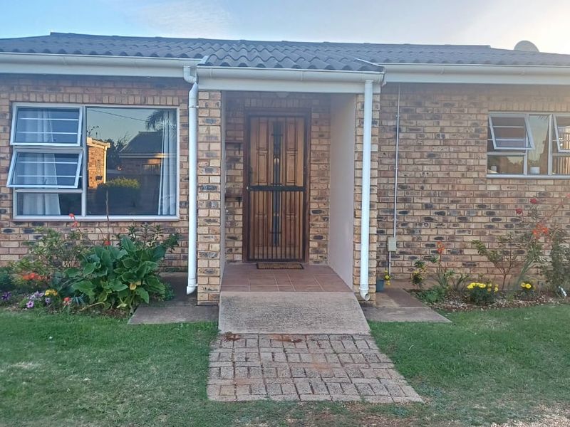 Front elevation of a face brick townhouse featuring a covered entrance, paved walkway, and aluminium window frames set within a landscaped garden.