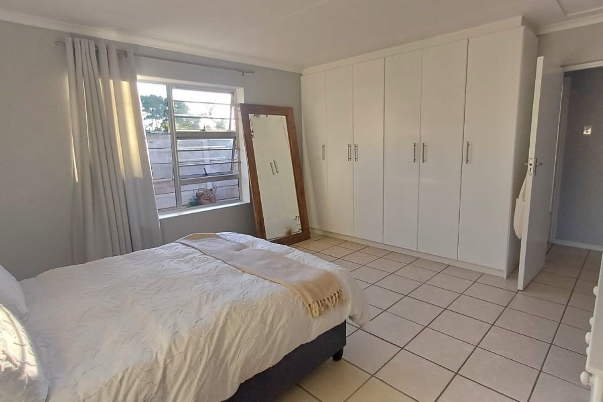 A well-maintained bedroom featuring neutral tiled flooring, ample built-in cupboard storage, and natural light through a large window.