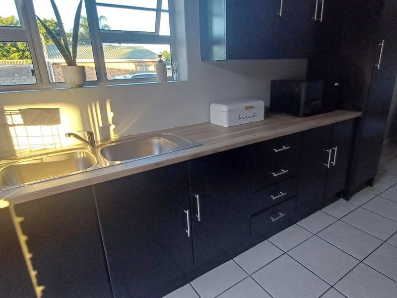 A modern kitchen featuring dark cabinetry, a light-toned laminate countertop, a double bowl stainless steel sink, and tiled flooring with natural light.