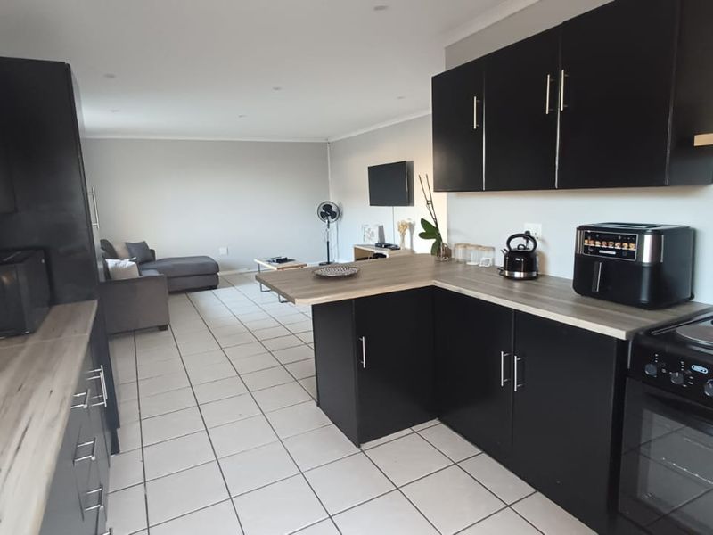 Open-plan kitchen and living area featuring modern black cabinetry, wood-look laminate countertops, tiled flooring, and a functional layout suitable for contemporary living.